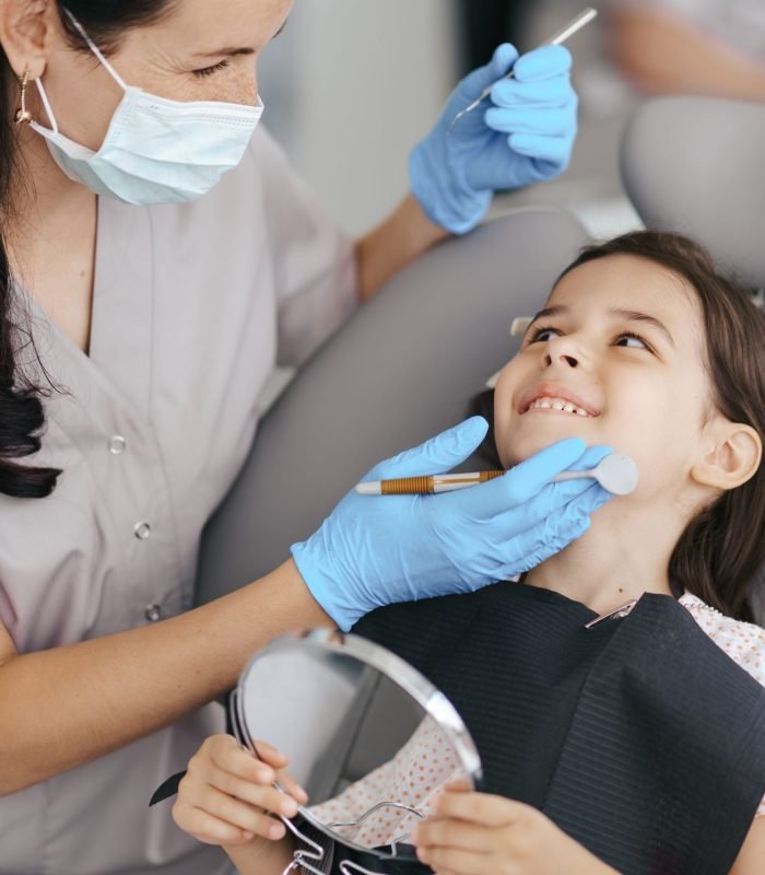 Cute little girl sitting on a modern dental chair and having dental consultation with dentist